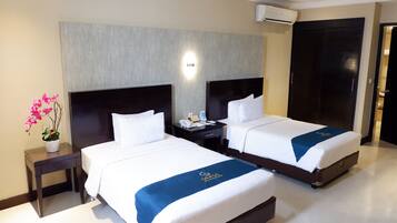 A hotel room with two beds, a nightstand, a potted plant, and a wall-mounted air conditioner.