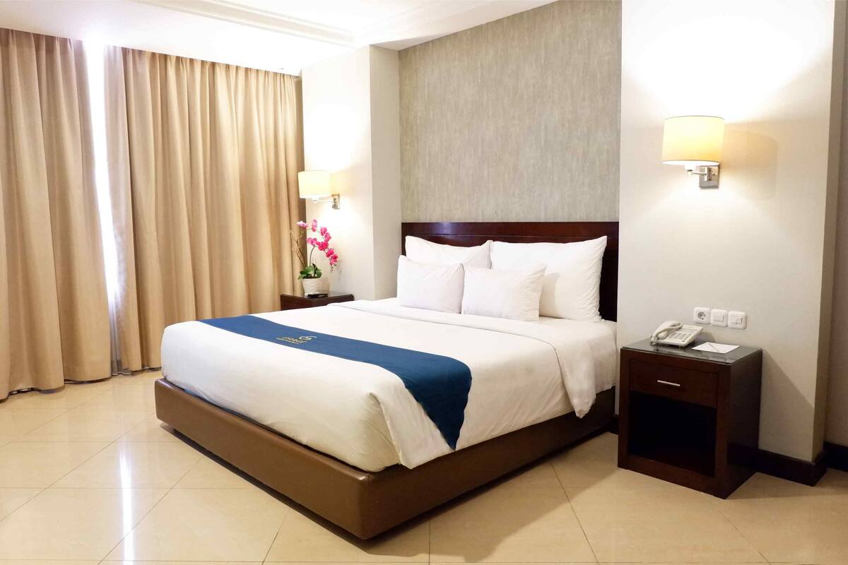 Una habitación de hotel con una cama grande, una mesita de noche con teléfono y una lámpara de pared.