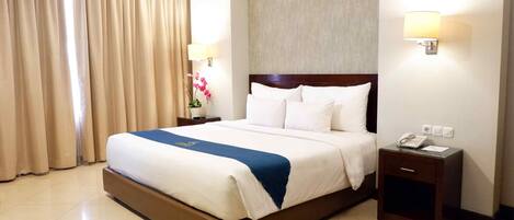 Una habitación de hotel con una cama grande, una mesita de noche con teléfono y una lámpara de pared.