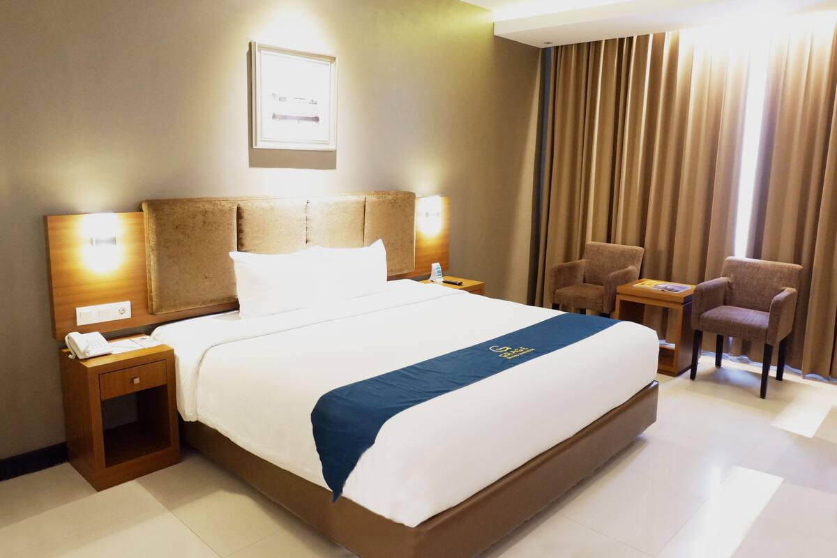 Habitación de hotel con una cama grande, mesitas de noche, un escritorio, una silla y una ventana con cortinas.