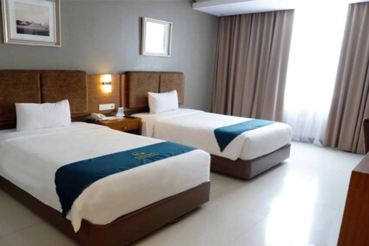 Una habitación de hotel con dos camas, una mesita de noche, una lámpara y una ventana con cortinas.