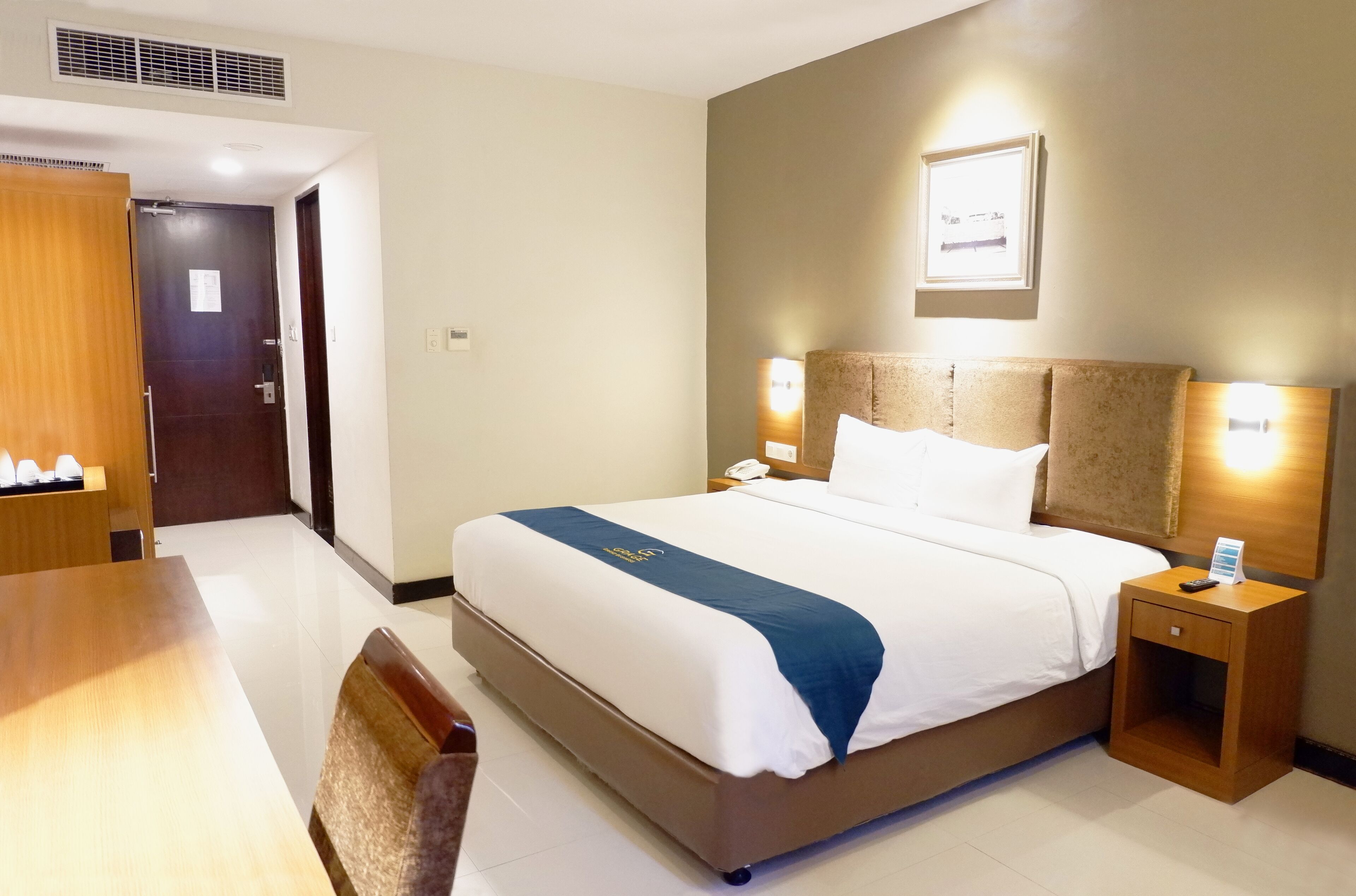 A hotel room with a bed, bedside table, nightstand, and a wooden chair.