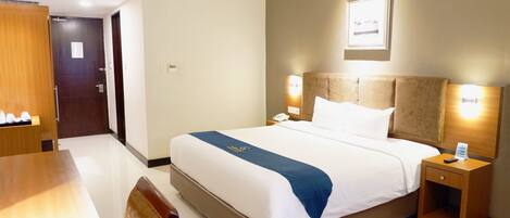A hotel room with a bed, bedside table, nightstand, and a wooden chair.