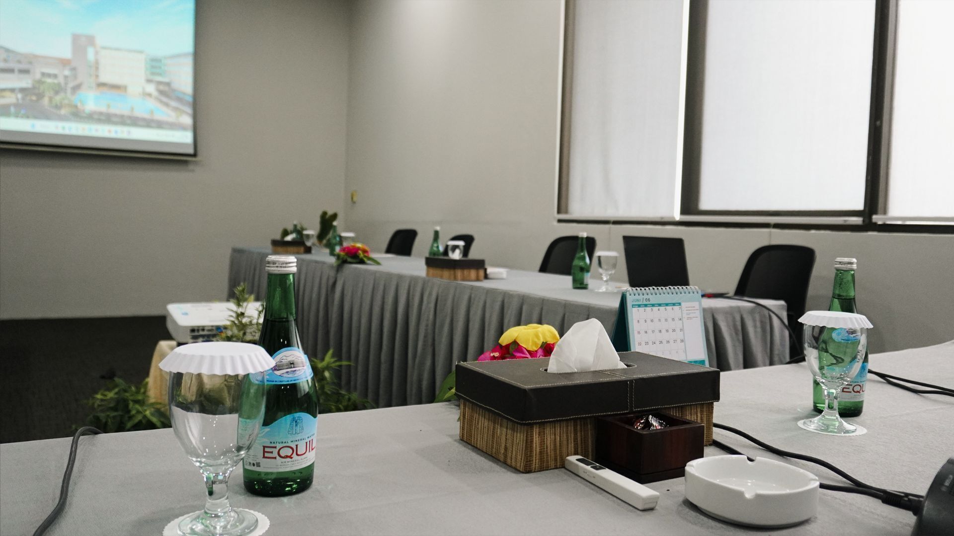 Une salle de conférence avec une table préparée pour une réunion, comprenant une boîte de mouchoirs, un calendrier et une bouteille d’eau.