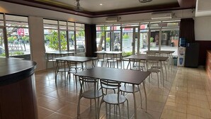 A restaurant interior with tables and chairs, a counter, and large windows. - Satria Cirebon (Cirebon)