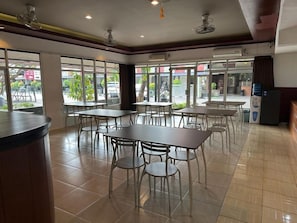 A restaurant interior with tables and chairs, a counter, and large windows. - Satria Cirebon (Cirebon)