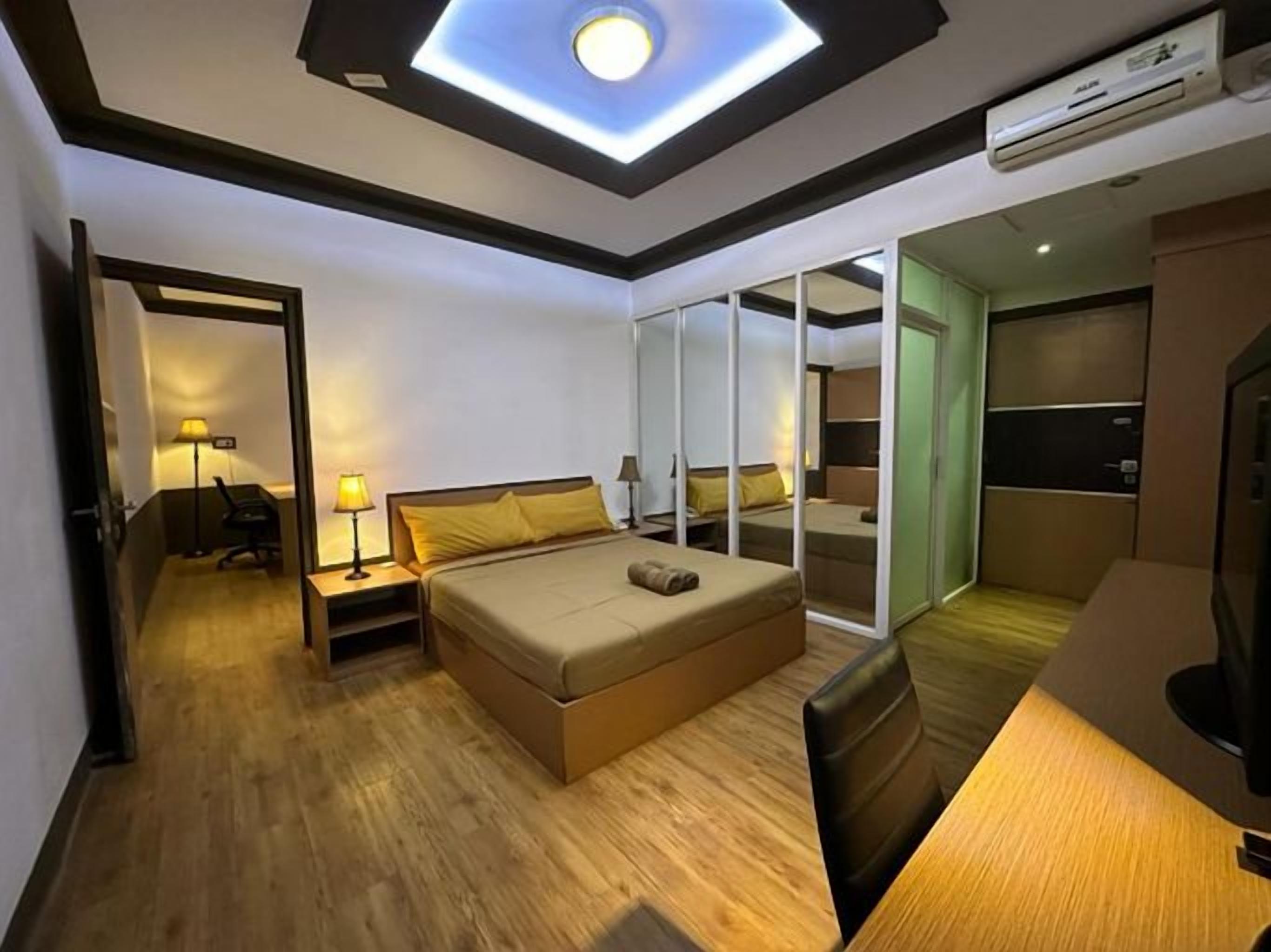A hotel room with a bed, bedside tables, a desk, and a ceiling light.