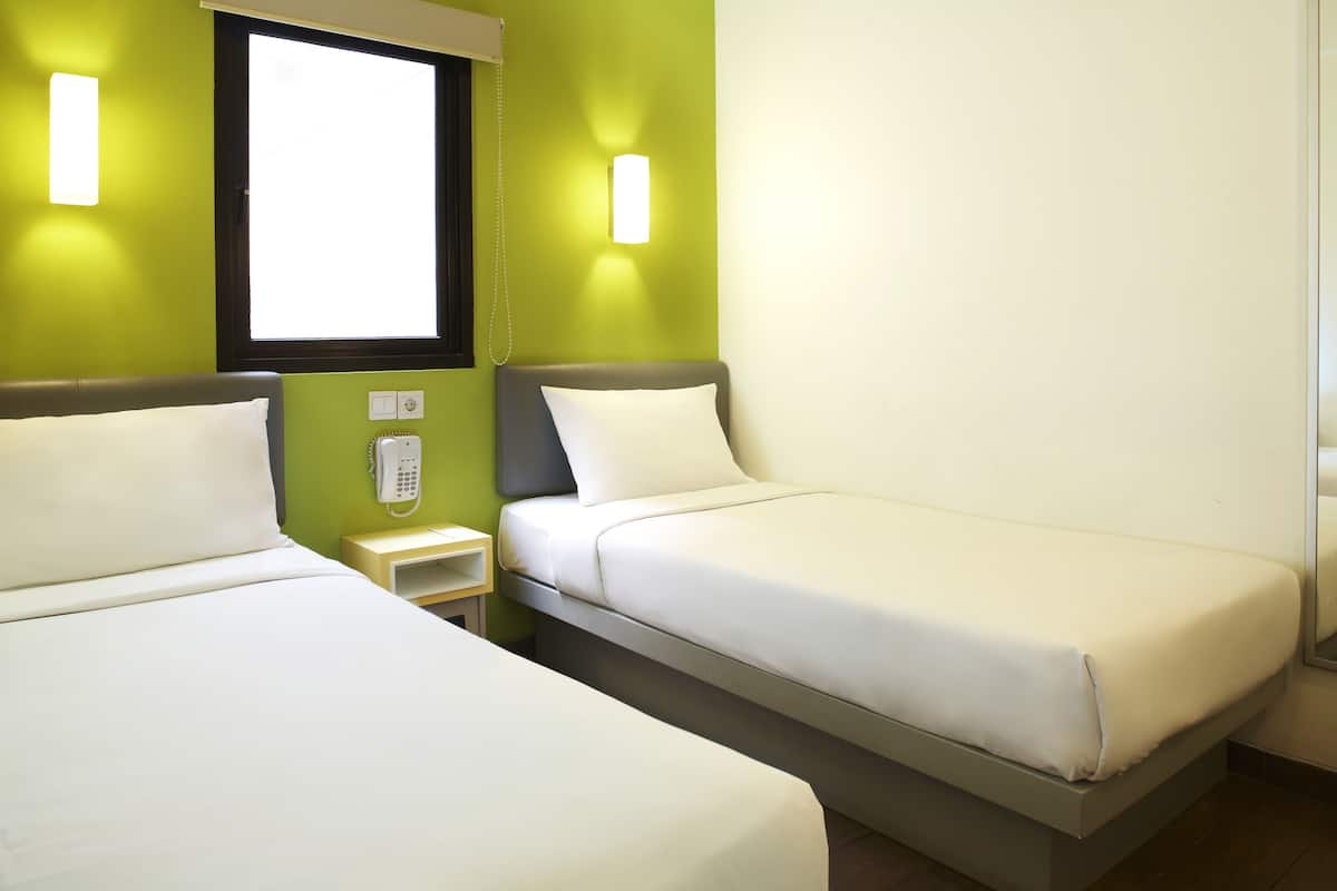 A hotel room with two single beds, a bedside table with a phone, and a window with blinds.