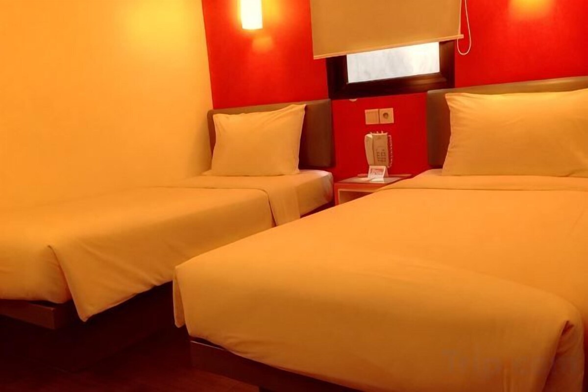 A hotel room with two single beds, a bedside table with a phone, and a red wall.
