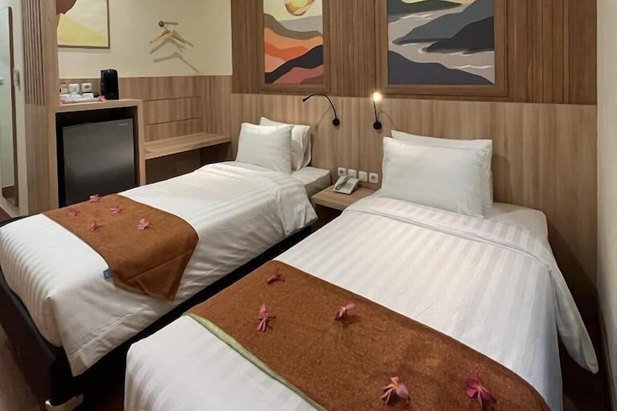 Habitación de hotel con dos camas, un escritorio, televisión y obras de arte en las paredes.