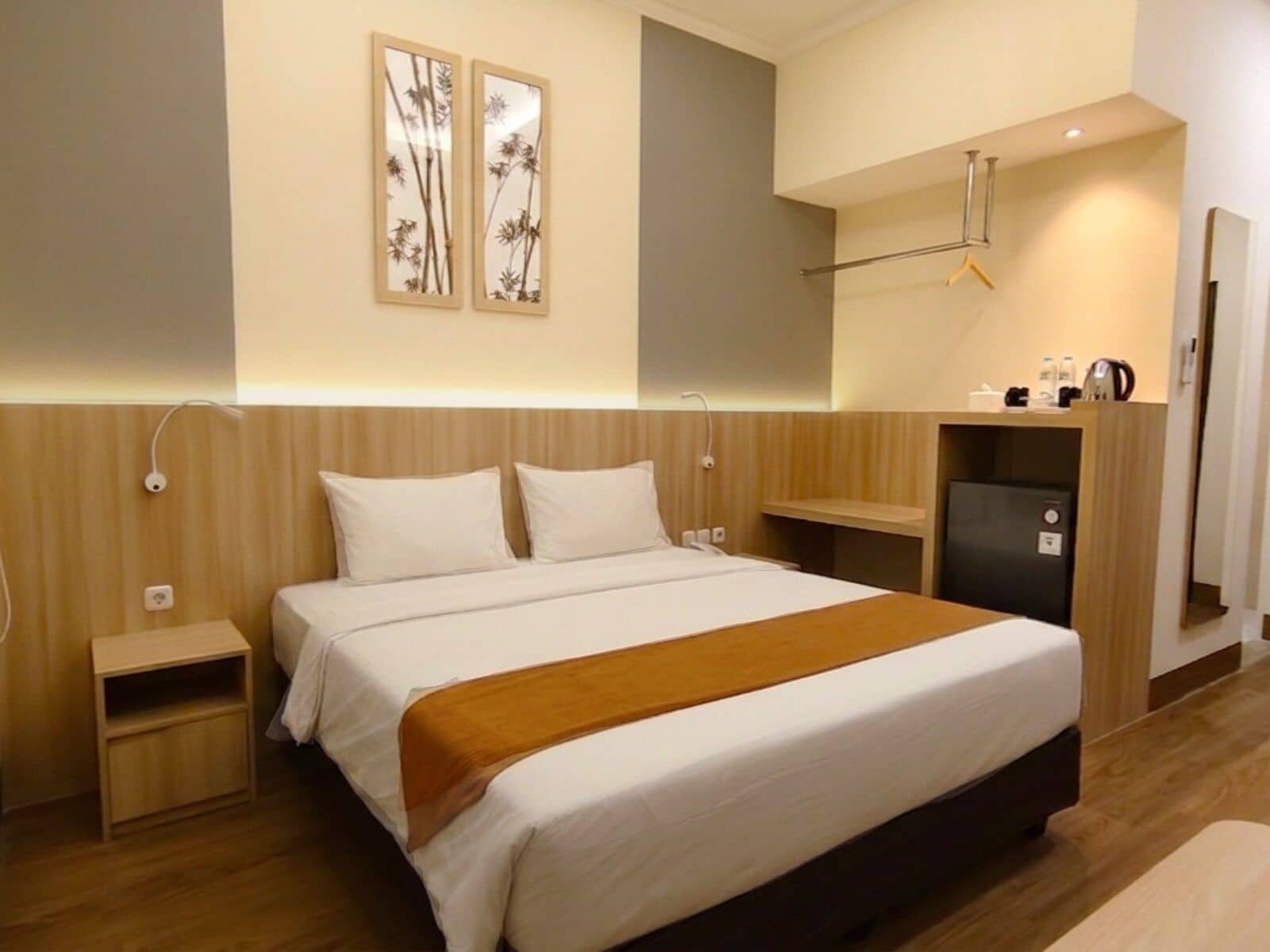 A hotel room with a bed, bedside tables, a small desk, and a mirror.