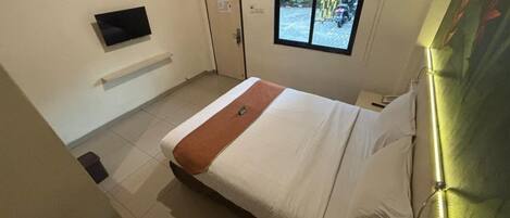 Una habitación de hotel con cama, televisor montado en la pared, ventana con vista a la calle y una puerta.