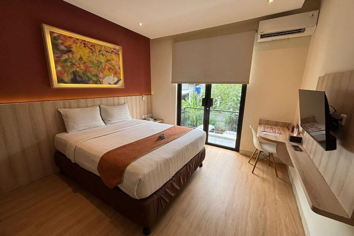 Una habitación de hotel con cama, escritorio, silla, televisor y balcón con vistas.