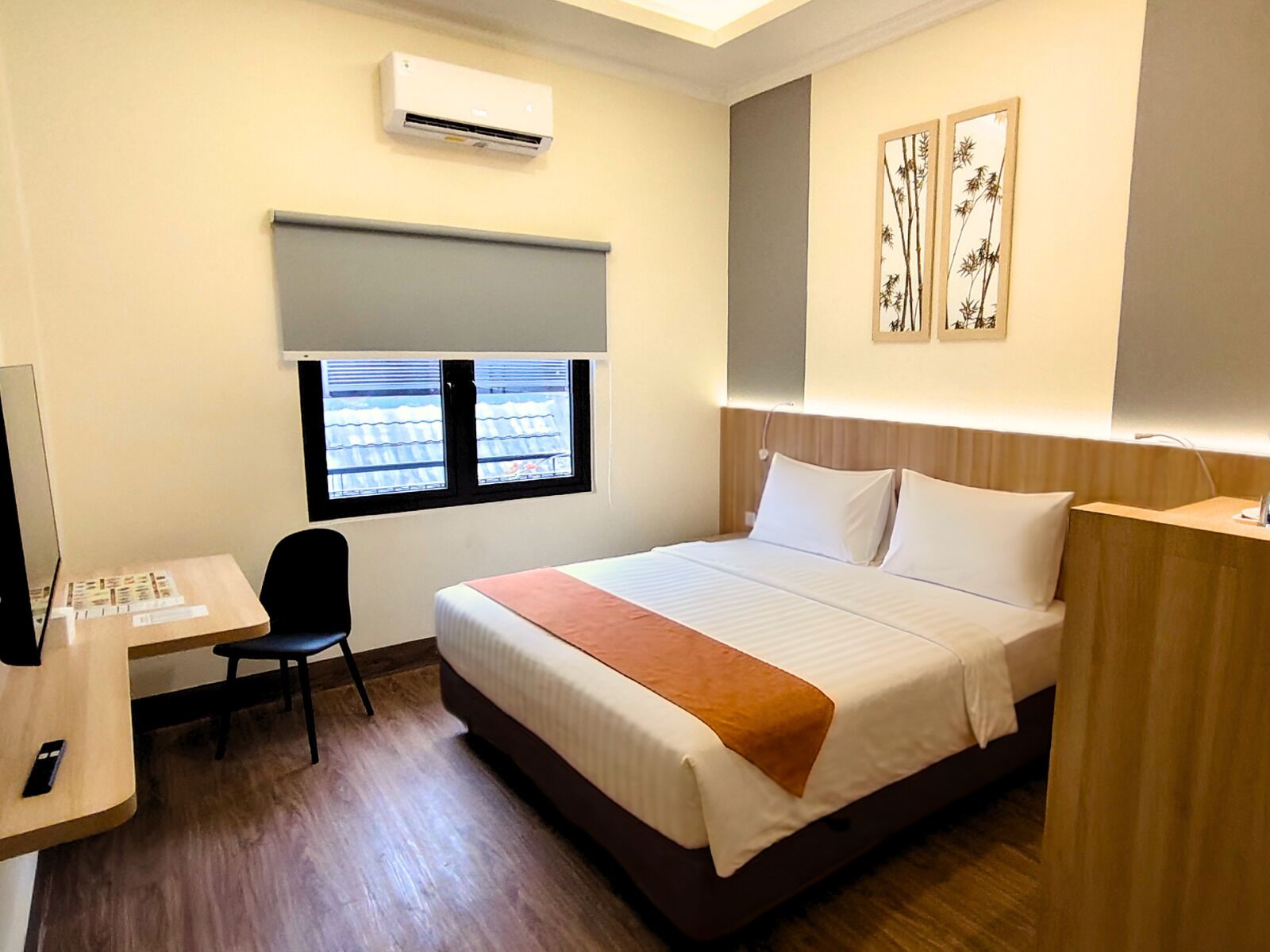 A hotel room with a bed, desk, chair, and a window with blinds.