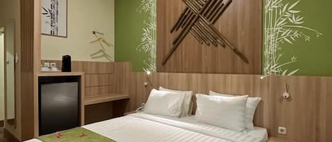 A neatly made bed with a green bedspread and white pillows, a wooden headboard with a decorative design, a small bedside table, and a wall-mounted light fixture.
