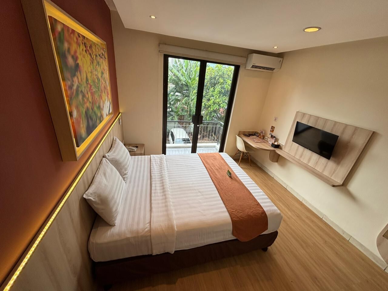 A modern hotel room with a large bed, a TV mounted on the wall, and a balcony with a view of greenery.