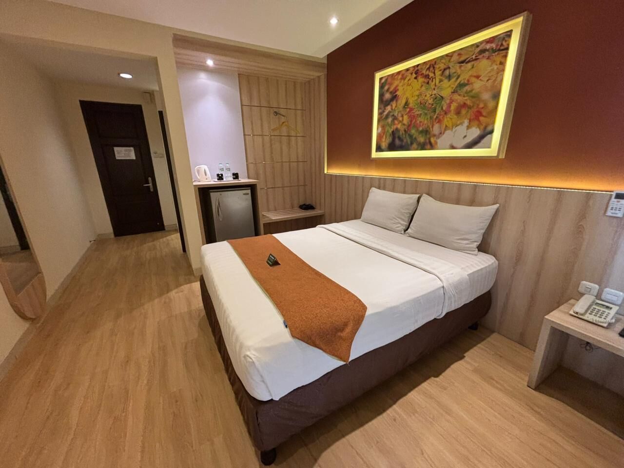 Une chambre d’hôtel avec un grand lit, une table de chevet avec un téléphone et un tableau au mur.