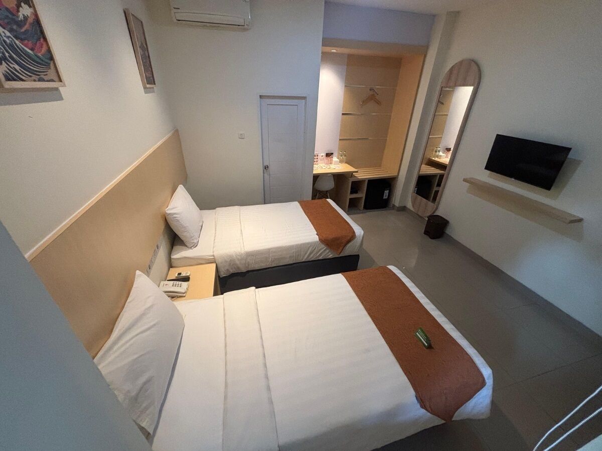 Hotellihuone, jossa on kaksi sänkyä, televisio, peili ja pieni työpöytä tuolilla.