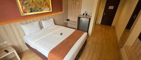 Una habitación de hotel con una cama, una mesita de noche, un escritorio pequeño, un espejo, un armario y una puerta.