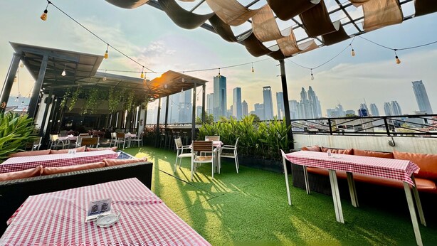 Un área de estar al aire libre con mesas y sillas, vista al horizonte de la ciudad y una estructura de pérgola.