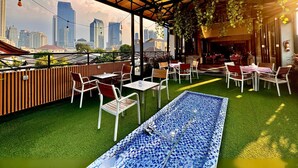 Un espacio al aire libre con mesas y sillas, una piscina pequeña y vistas al horizonte de la ciudad.