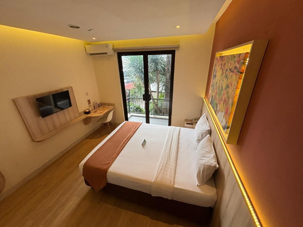 Una habitación de hotel moderna con una cama grande, un escritorio, una silla y una ventana con vistas a palmeras.