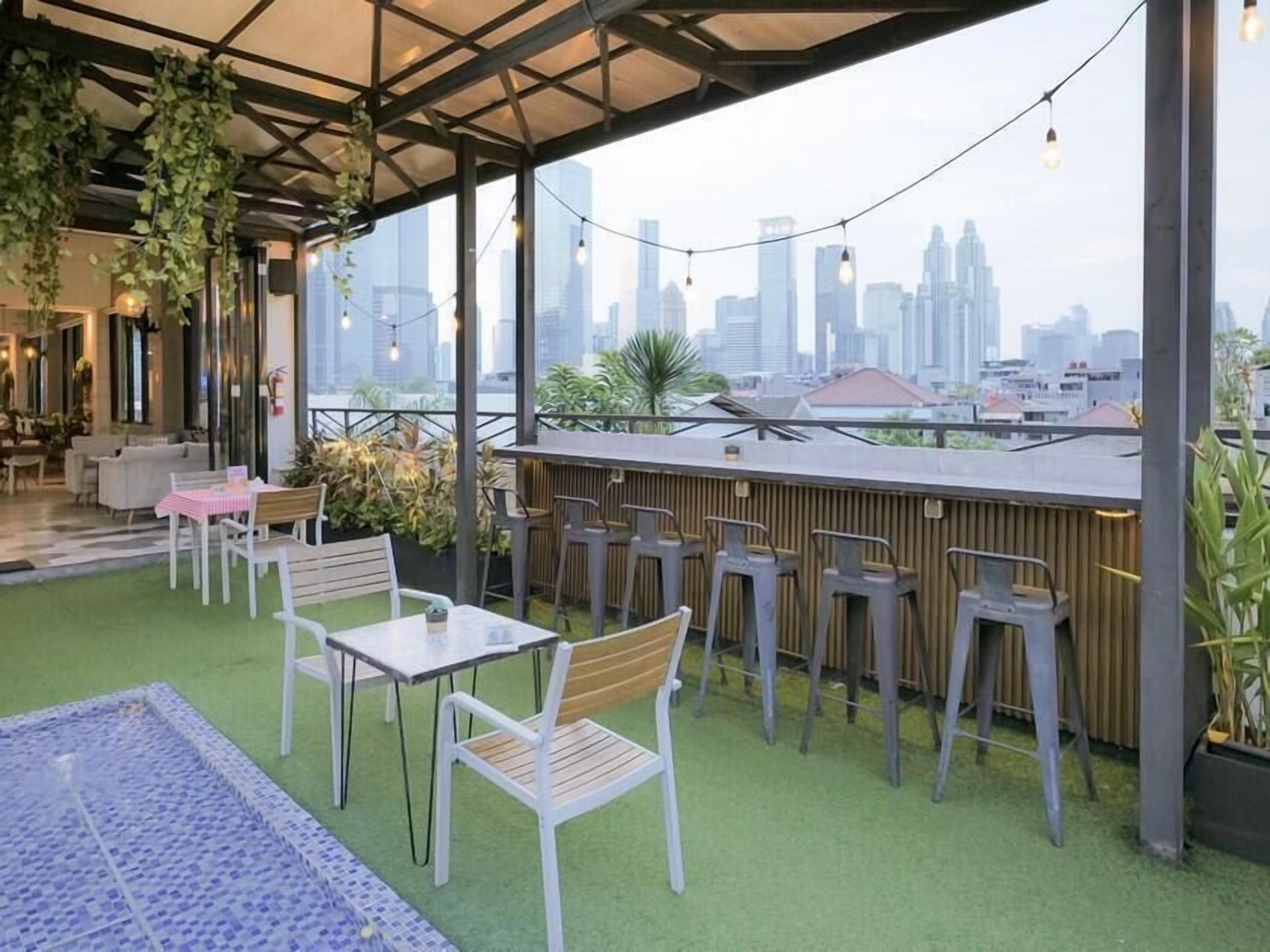 An outdoor seating area with tables and chairs, a view of the city skyline, and string lights.