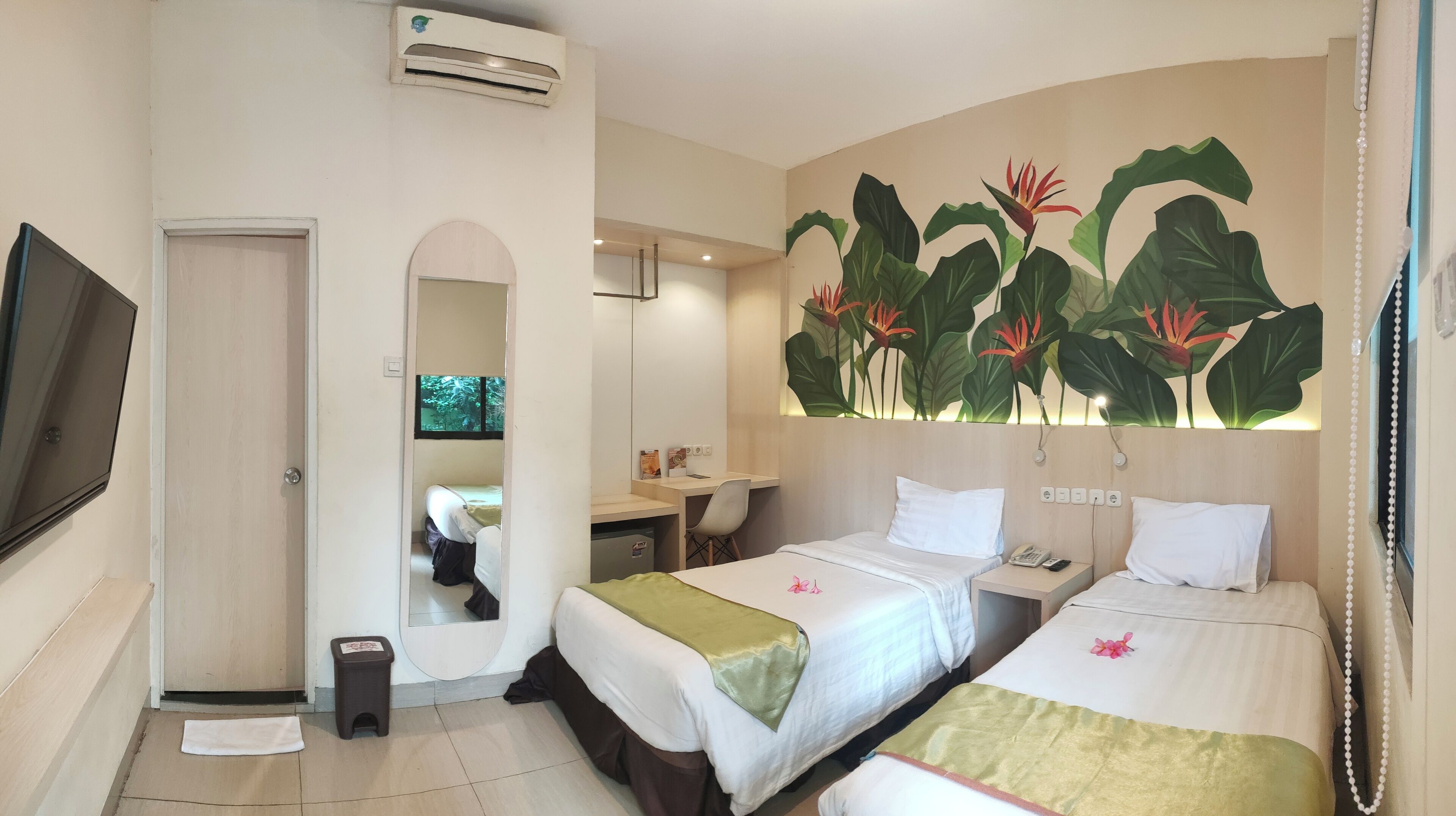 A hotel room with two beds, a desk, a chair, a TV, and a large tropical mural.