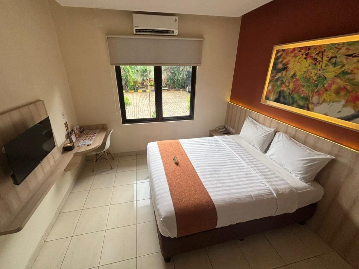 Habitación de hotel con cama, escritorio, televisión y ventana con vista al exterior.