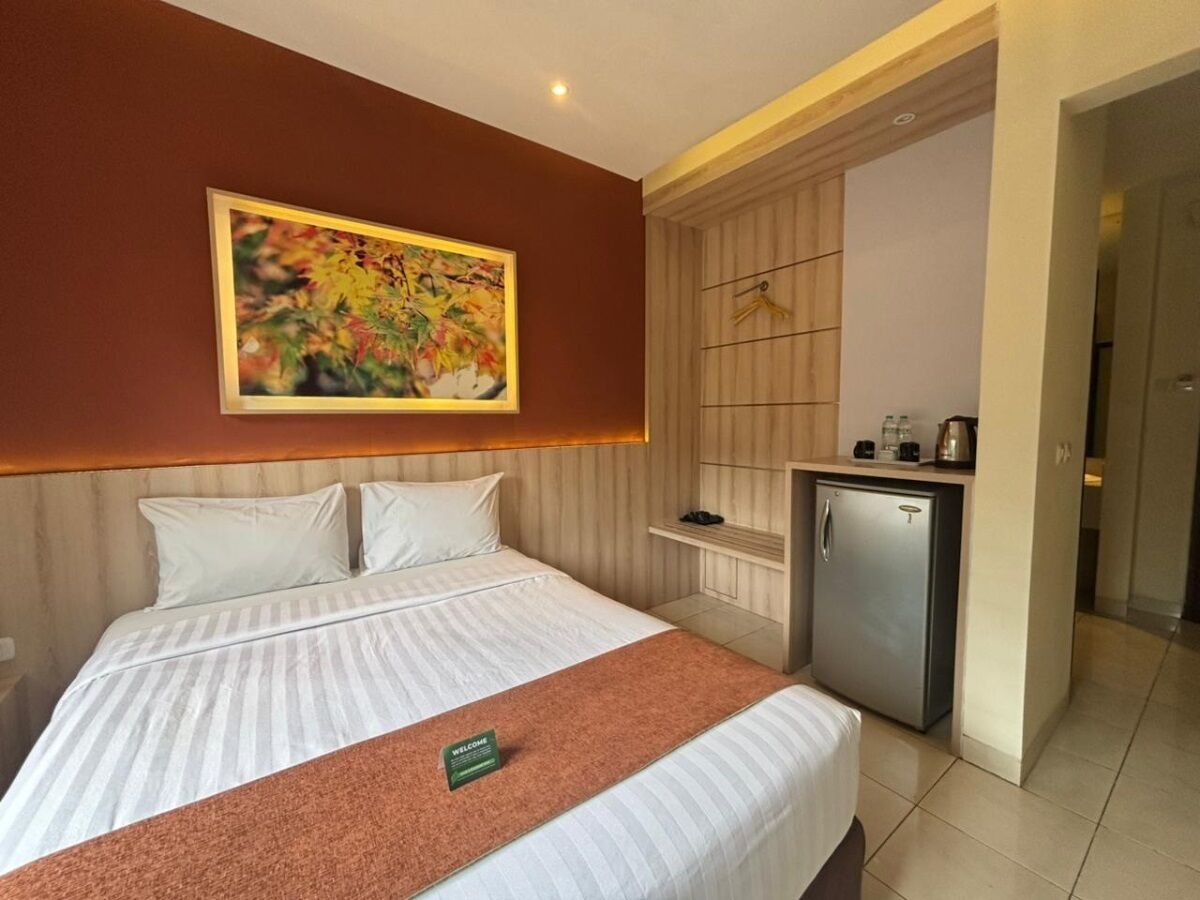 Habitación de hotel con una cama, un pequeño kitchenette, un cuadro en la pared y un cartel de bienvenida sobre la cama.