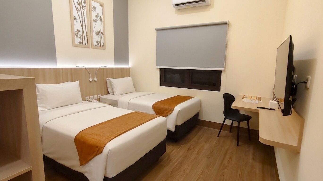 Une chambre d’hôtel avec deux lits, un bureau, une chaise, un climatiseur et une télévision.