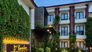 Entrada de un hotel con un cartel que dice "D'Banosa Suites", rodeada de abundante vegetación y un camino pavimentado.