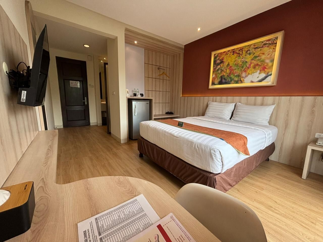 Ein Hotelzimmer mit einem Bett, einem Schreibtisch mit Stuhl, einem an der Wand montierten Fernseher und einem Gemälde über dem Bett.