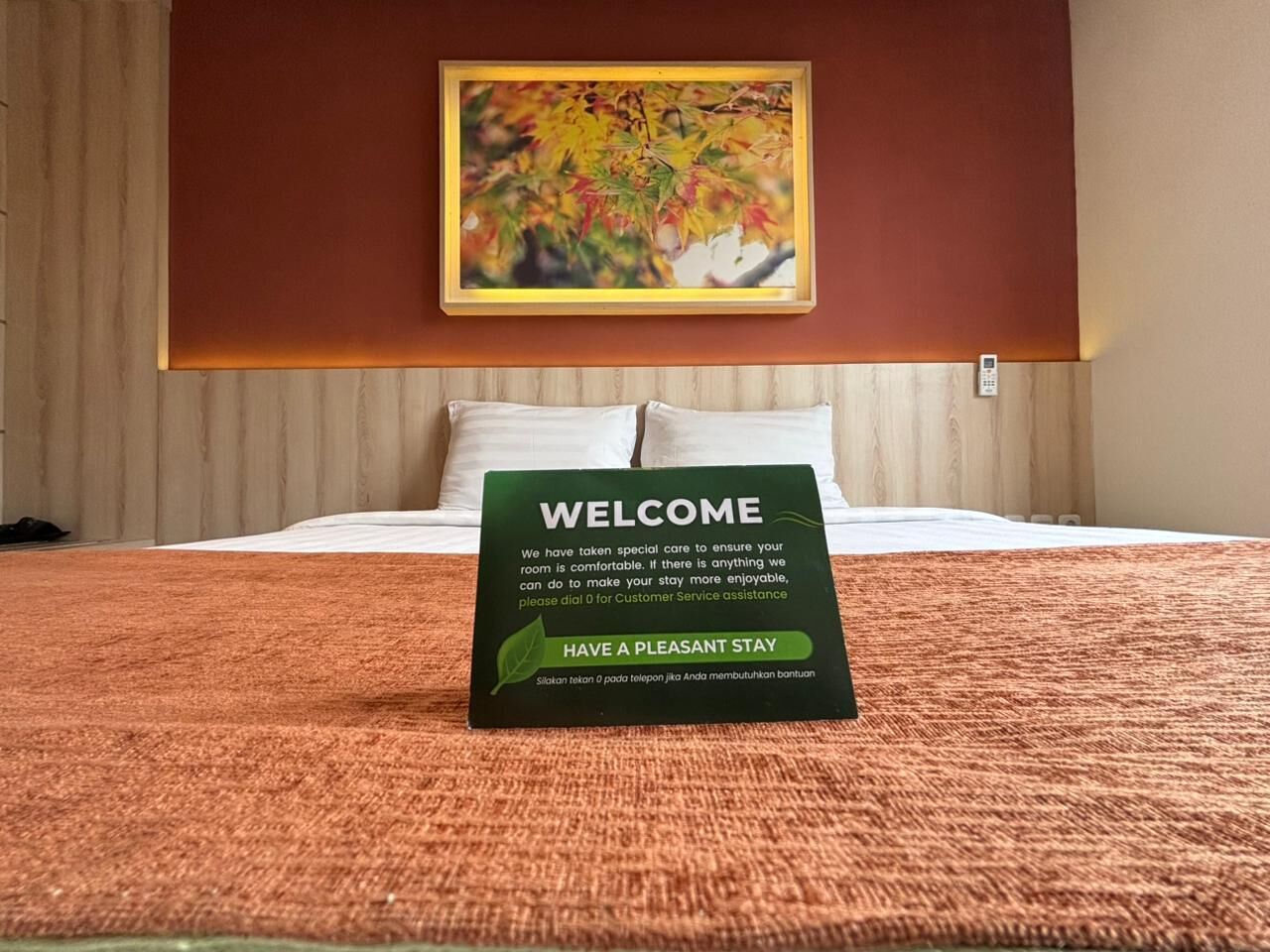 A hotel room with a welcome sign on the bed, a painting on the wall, and a telephone on the nightstand.