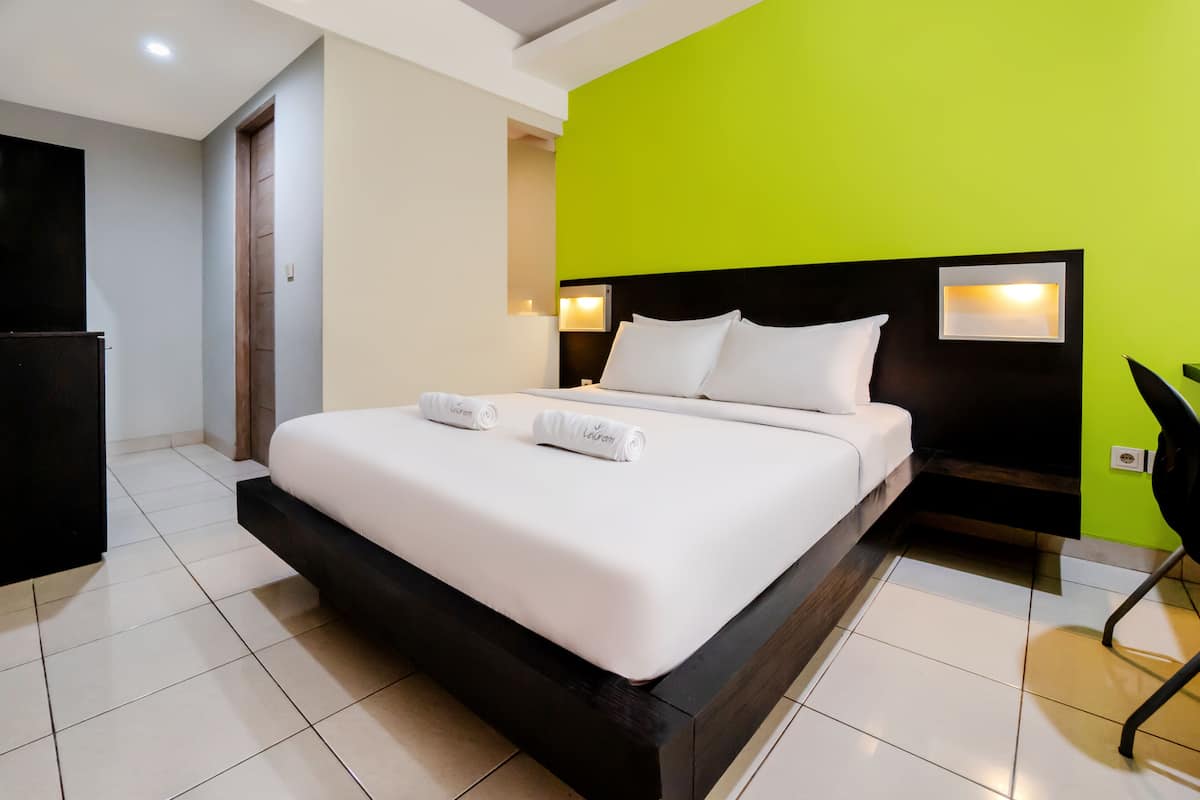 A modern hotel room with a large bed, a nightstand, a TV, and a bright green accent wall.