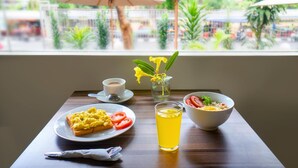 Una mesa de desayuno con huevos revueltos, tostadas y tomates, un bol de cereal, un vaso de bebida amarilla y una taza de café.