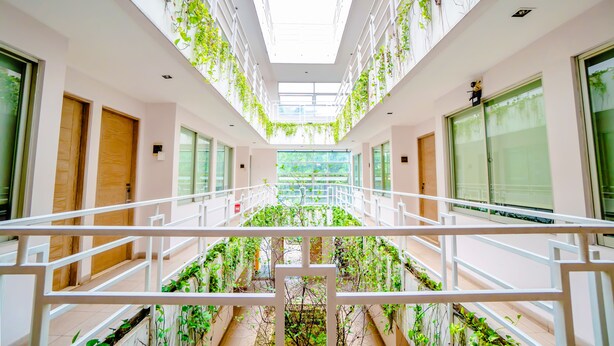 Un interior moderno con un atrio central, barandillas blancas y plantas verdes.