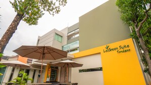 Un edificio con fachada amarilla y blanca, mesas al aire libre con sombrillas, y un letrero que dice