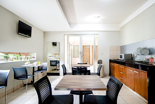 Una cocina moderna con comedor, que incluye una mesa y sillas de madera, un televisor en la pared y vistas al exterior a través del ventanal.