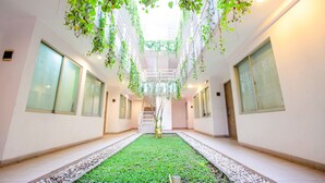 Un pasillo con un área verde central, paredes blancas y plantas colgantes.