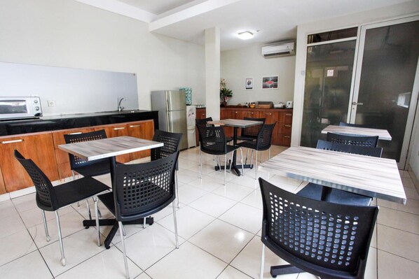 A modern kitchen with a microwave, refrigerator, and dining area with black chairs and a white table. - LeGreen Suite Tondano (Jakarta)