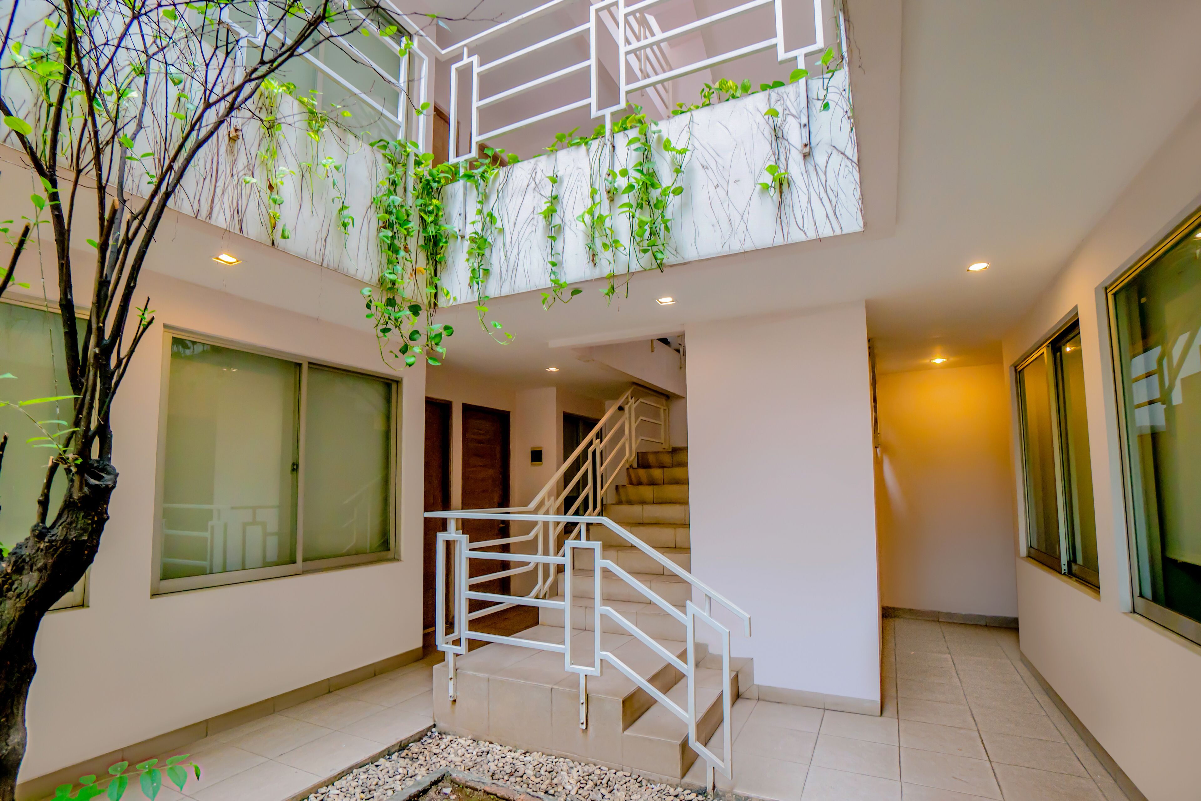 Un intérieur moderne avec un escalier, un arbre et un balcon agrémenté de plantes.