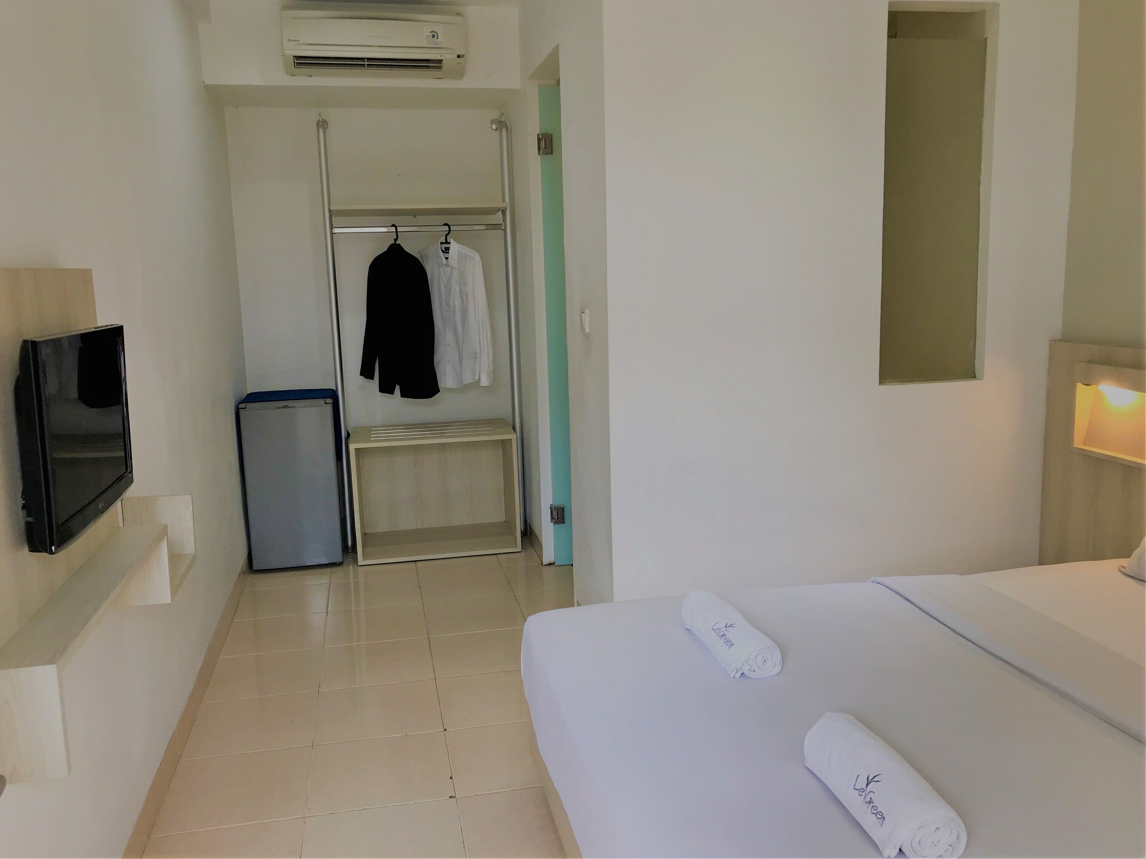 Una habitación de hotel con cama, televisión, armario y un cubo de basura pequeño.