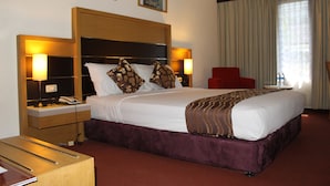 A hotel room with a large bed, two bedside tables with lamps, a red chair, and a window with curtains. - Mega Matra Hotel (Jakarta)