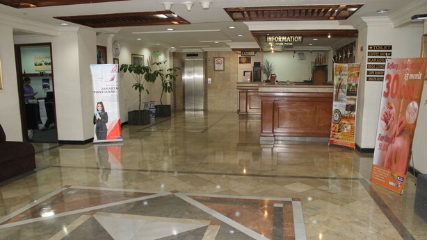A hotel lobby with a reception desk, a cashier, a sign for the information house, and a poster advertising a 15-minute wait for a 30,000 menu. - Mega Matra Hotel (Jakarta)