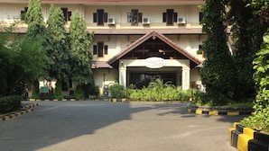 A building with a tiled roof, a sign above the entrance, and a paved driveway leading to the entrance. - Mega Matra Hotel (Jakarta)