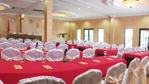 Sala de conferência com várias mesas preparadas para uma reunião, cada uma com toalha vermelha e capas brancas para as cadeiras.