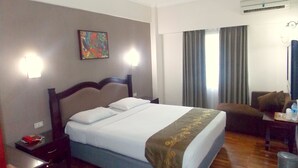 Quarto de hotel com cama, secretária, cadeira e um quadro na parede.