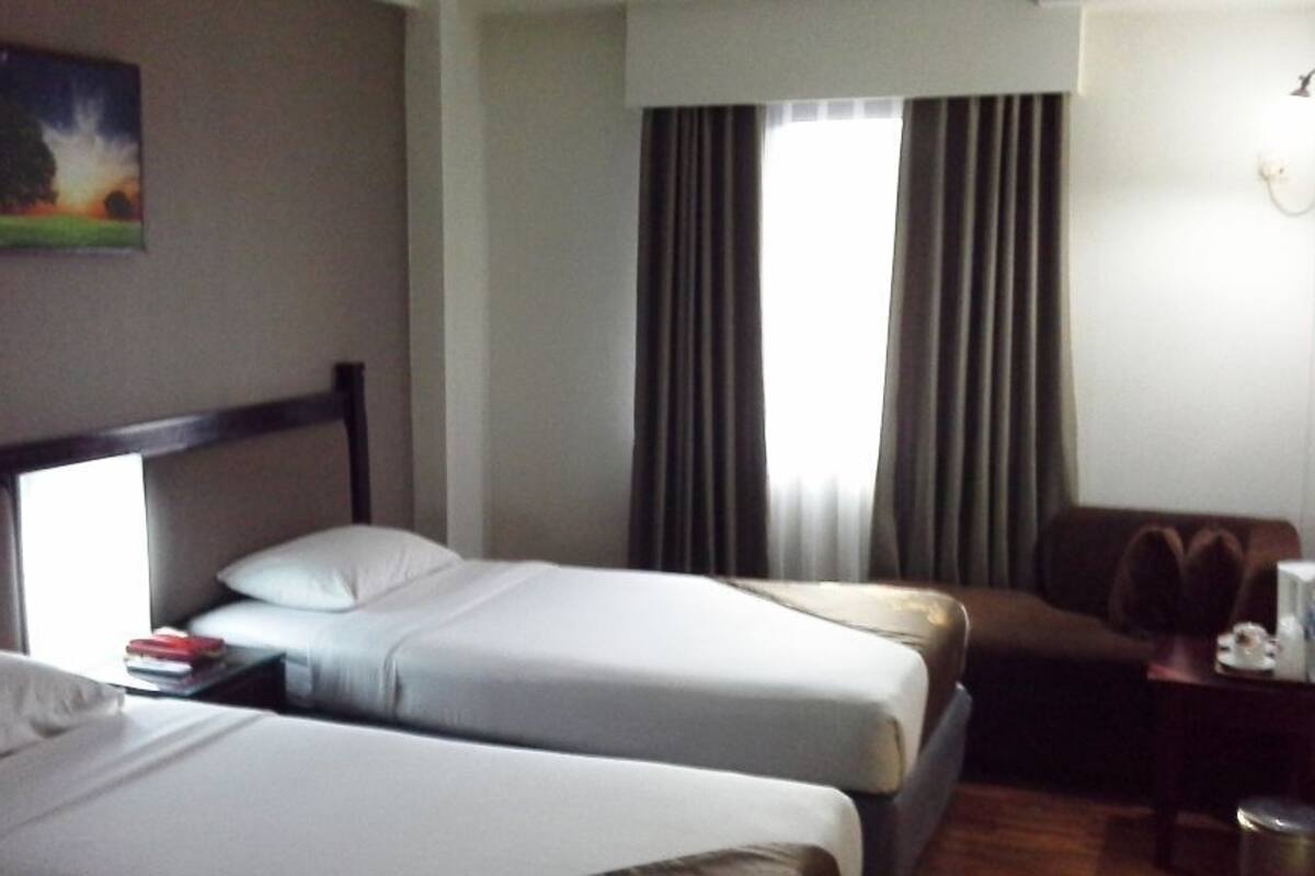 Ein Hotelzimmer mit zwei Betten, einem Schreibtisch, einem Stuhl, einem Bild an der Wand und einem Fenster mit Vorhängen.