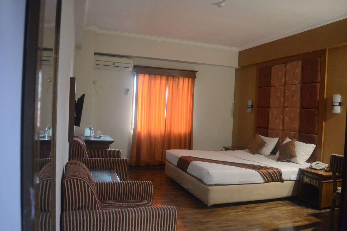 Ein Hotelzimmer mit einem Bett, einer Sitzecke mit Stühlen, einem Schreibtisch mit Stuhl und einem Fenster mit Vorhängen.